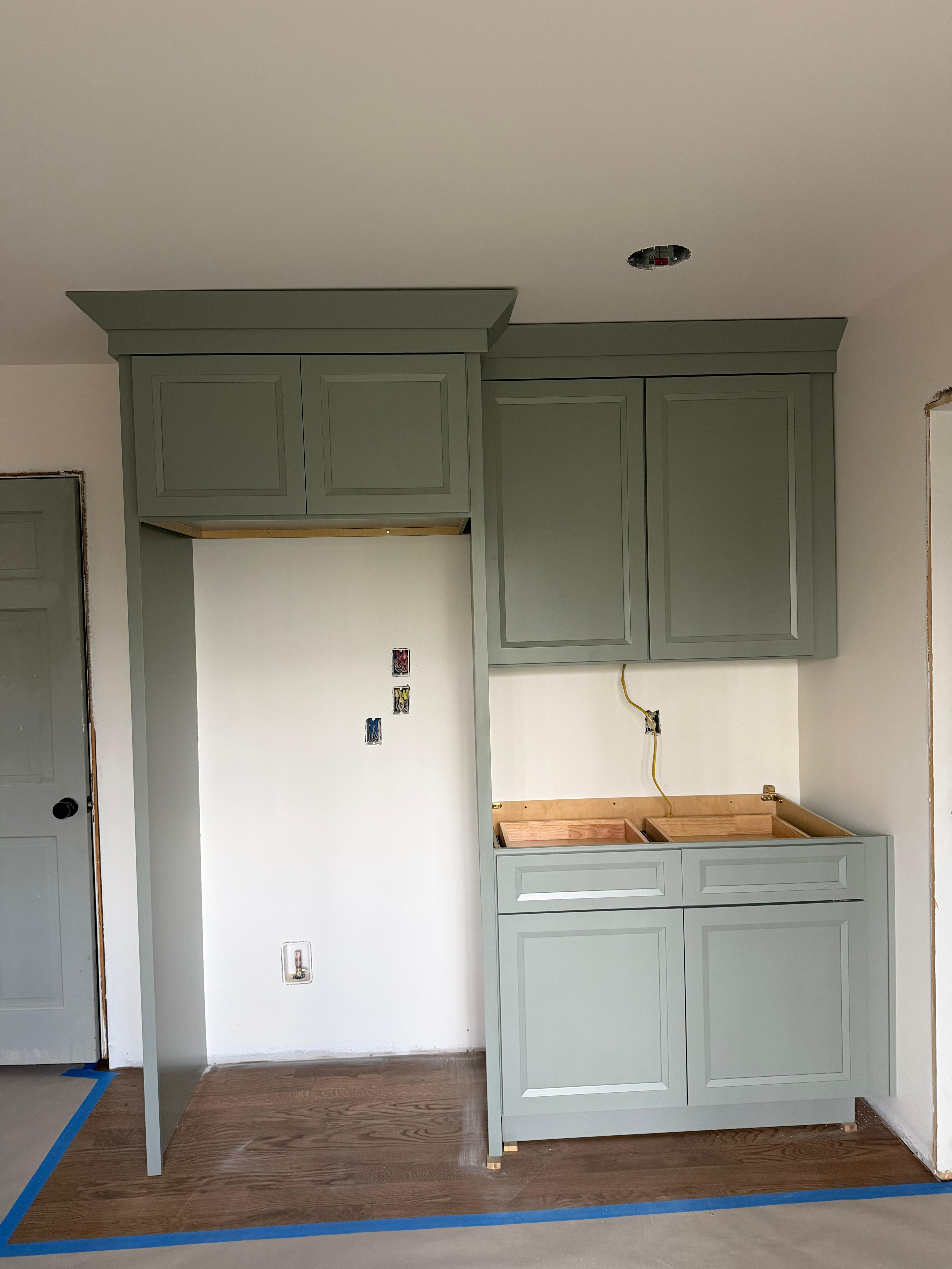 Sage cabinetry and trim during installation; countertops and final work are still pending.