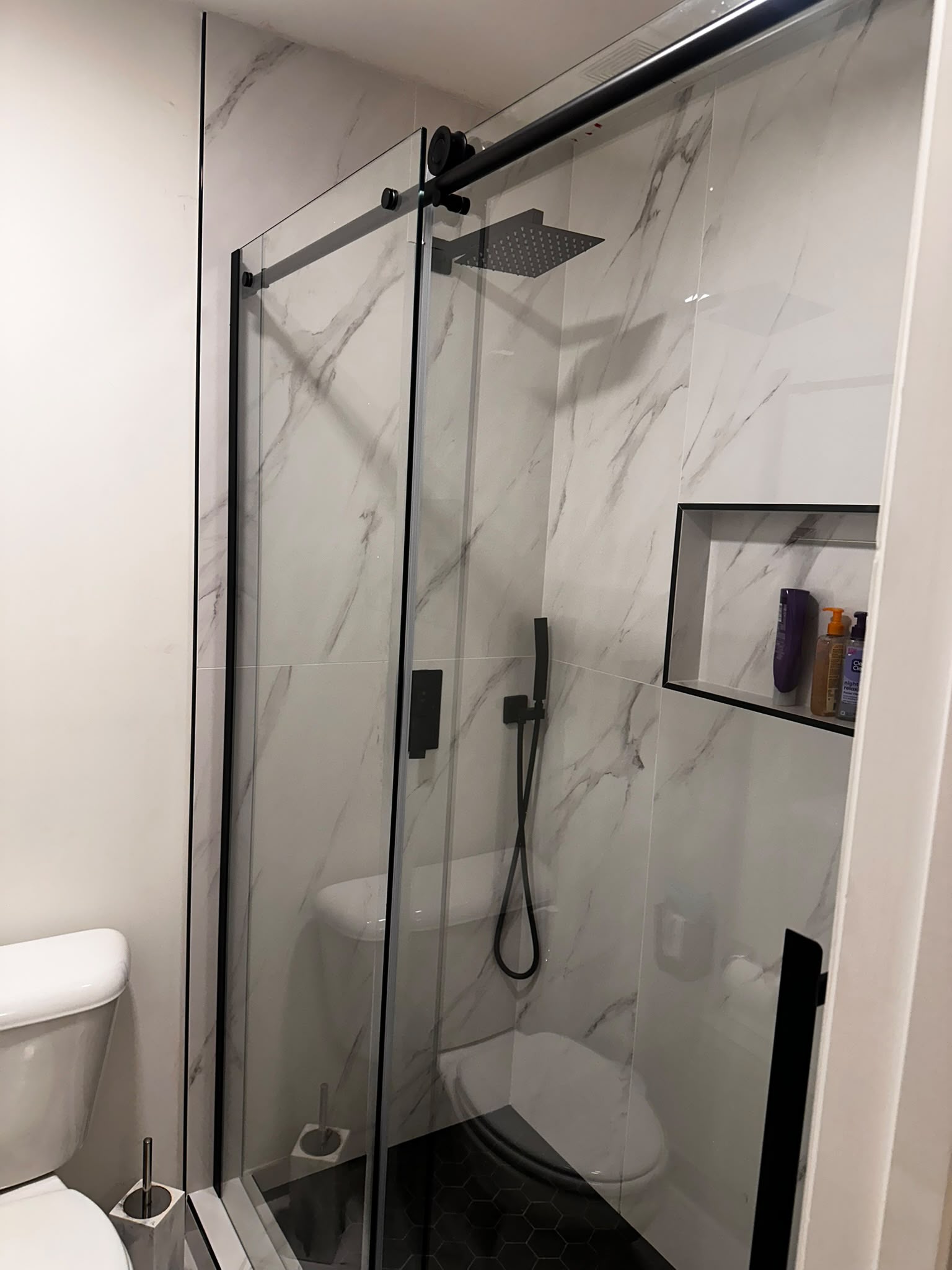 Glass shower enclosure with dark hardware and large-format wall tile.