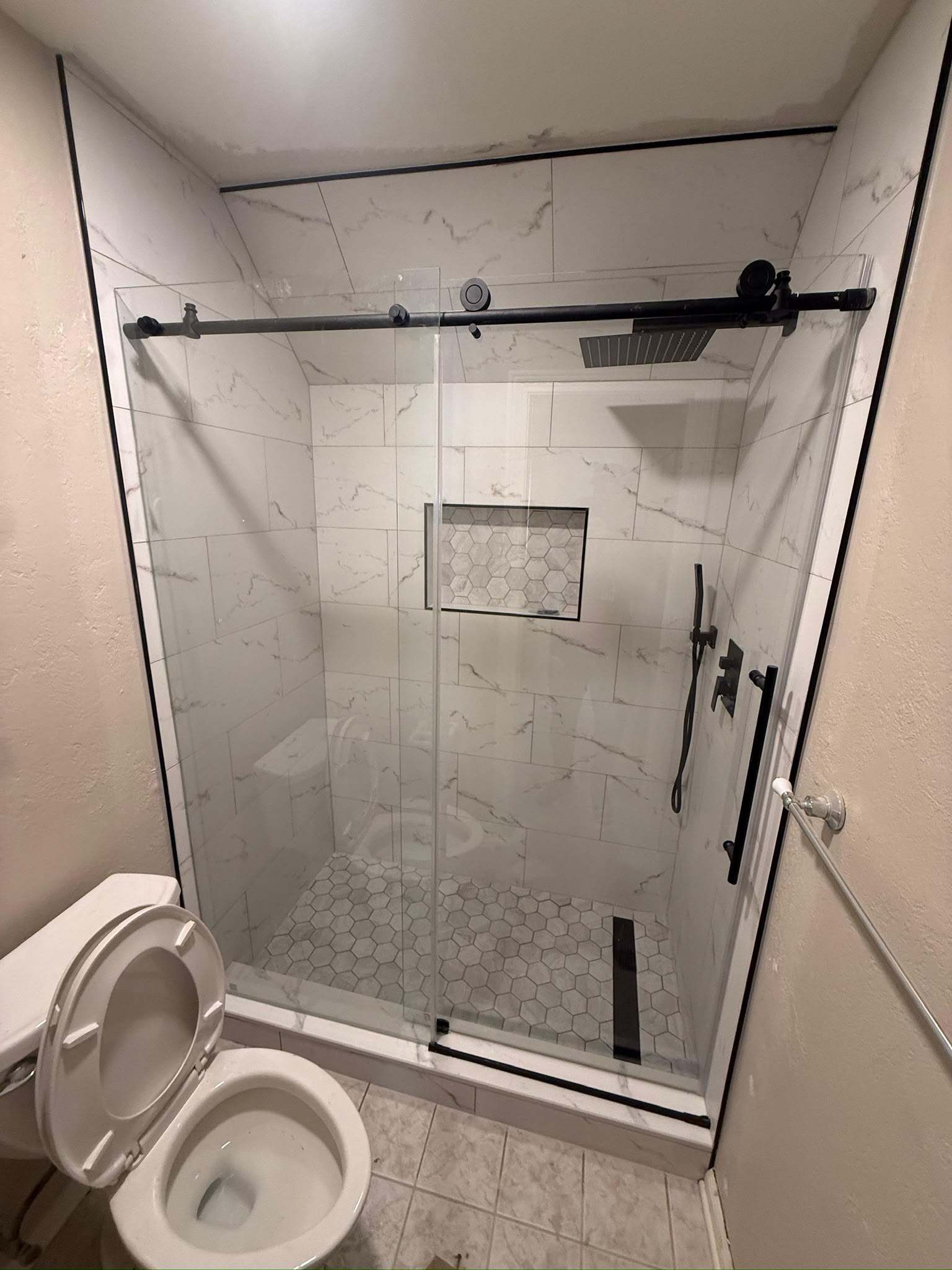Sliding glass shower enclosure, recessed niche and contrasting dark hardware.
