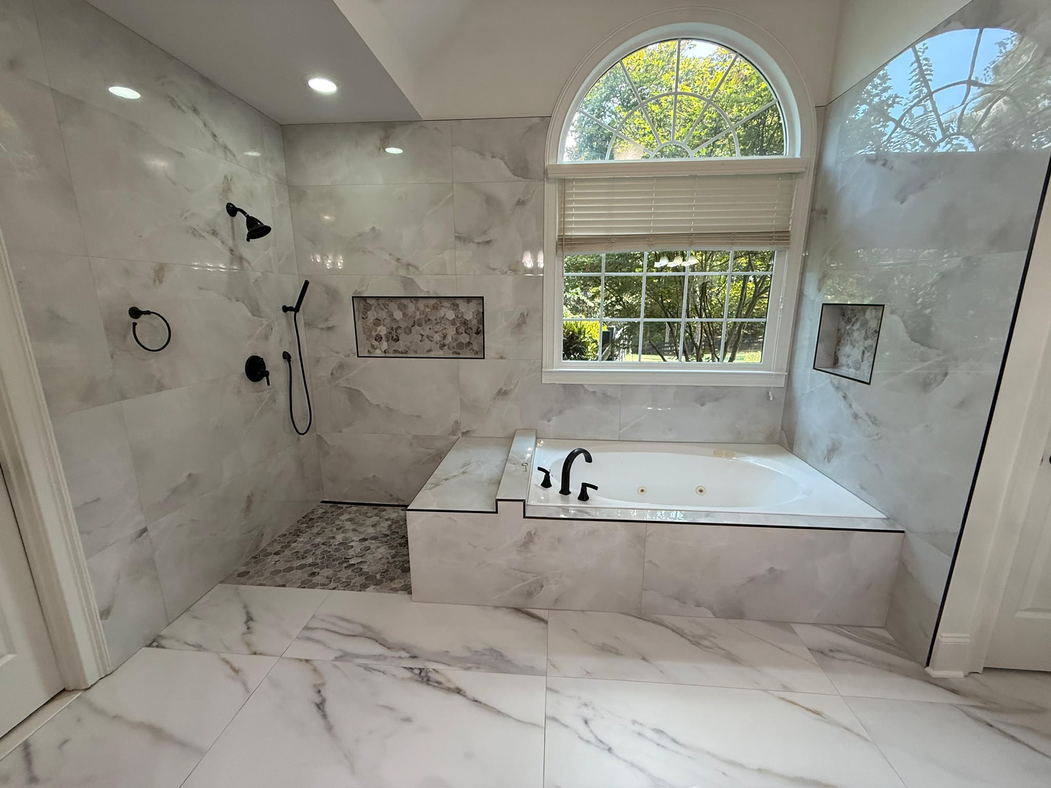 Peachline tub and shower with marble-look surfaces, recessed niches and black fixtures